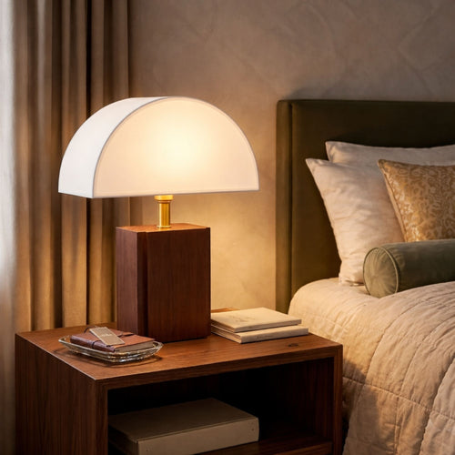 Bordslampa med vit skärm och träfot placerad på nattduksbord i sovrum som ger ett varmt och mysigt ljus